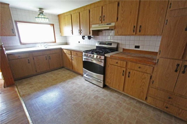 kitchen featuring light countertops, light floors, under cabinet range hood, stainless steel gas stove, and backsplash