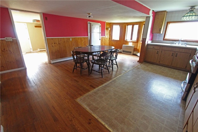 dining space featuring light wood-type flooring, wooden walls, a baseboard radiator, and plenty of natural light