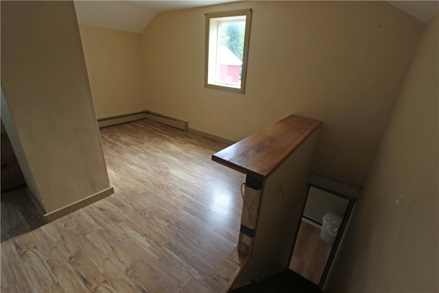 additional living space featuring a baseboard radiator, light hardwood / wood-style floors, and vaulted ceiling