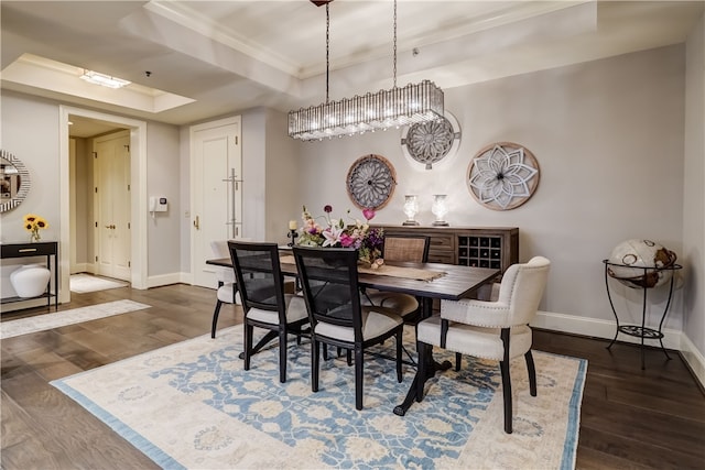 dining room with crown molding, a tray ceiling, and dark wood-type flooring