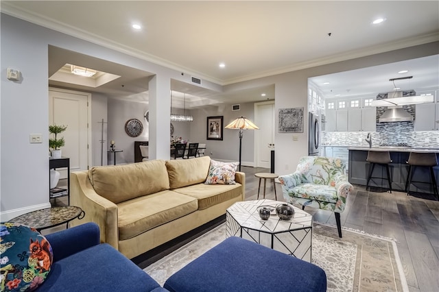 living room with light wood-type flooring, crown molding, an inviting chandelier, and a raised ceiling