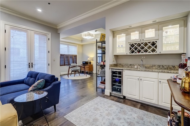 bar with dark wood-type flooring, wine cooler, white cabinets, ornamental molding, and sink