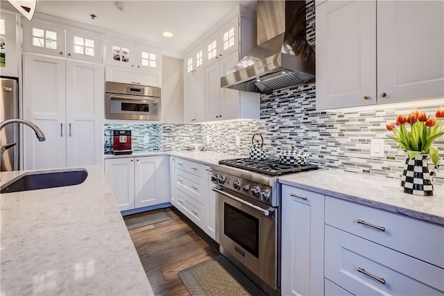 kitchen featuring light stone counters, tasteful backsplash, white cabinets, stainless steel appliances, and wall chimney range hood