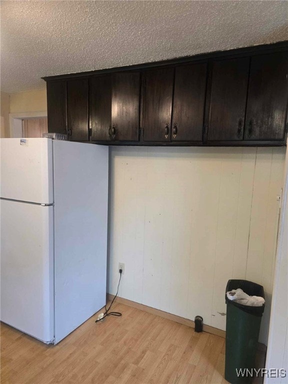 kitchen with dark brown cabinetry, white refrigerator, light wood-type flooring, and a textured ceiling