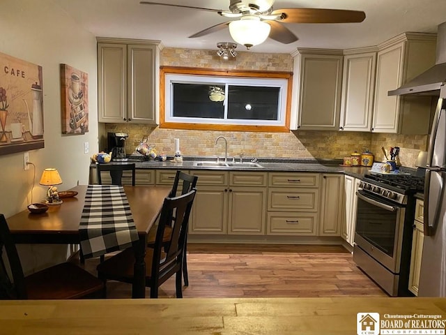 kitchen featuring wall chimney exhaust hood, sink, appliances with stainless steel finishes, light hardwood / wood-style floors, and cream cabinetry