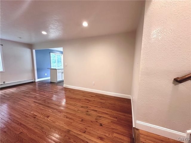 spare room featuring baseboard heating and dark hardwood / wood-style flooring