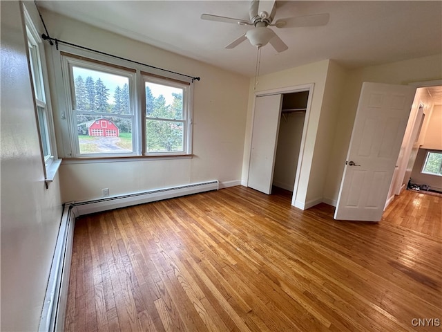 unfurnished bedroom featuring baseboard heating, ceiling fan, a closet, and hardwood / wood-style flooring