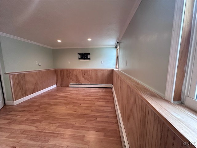 empty room with light hardwood / wood-style flooring, a baseboard heating unit, and ornamental molding