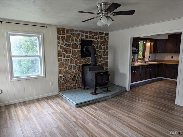 unfurnished living room featuring ceiling fan, light hardwood / wood-style flooring, sink, and a wood stove