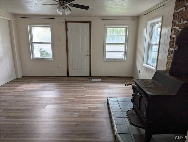 entryway with ceiling fan, plenty of natural light, light hardwood / wood-style floors, and a wood stove