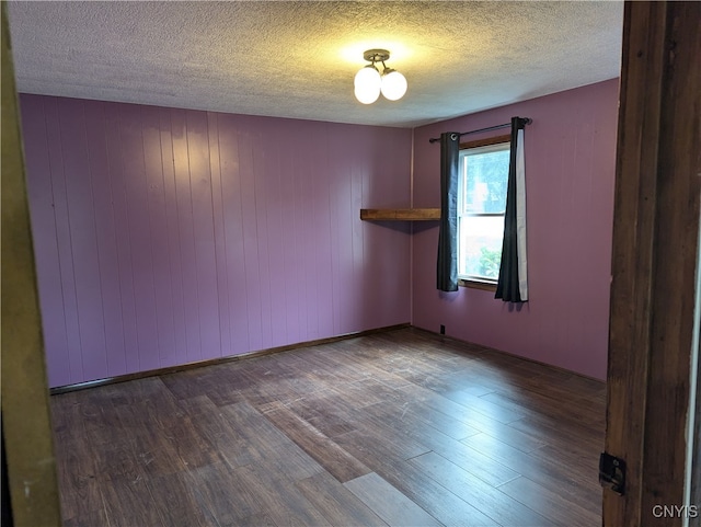 unfurnished room with wooden walls, a textured ceiling, and hardwood / wood-style flooring