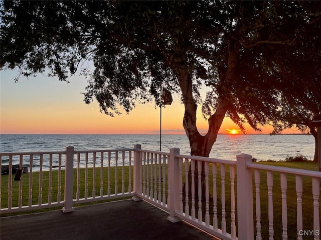 patio terrace at dusk featuring a lawn and a water view