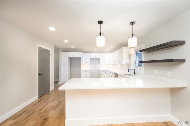 kitchen featuring light wood-type flooring, kitchen peninsula, white cabinetry, and sink