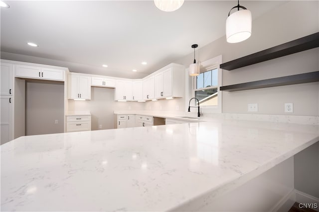 kitchen featuring hanging light fixtures, white cabinets, sink, and light stone countertops