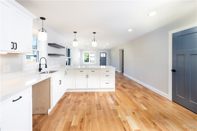 kitchen with hanging light fixtures, white cabinetry, kitchen peninsula, light hardwood / wood-style flooring, and sink