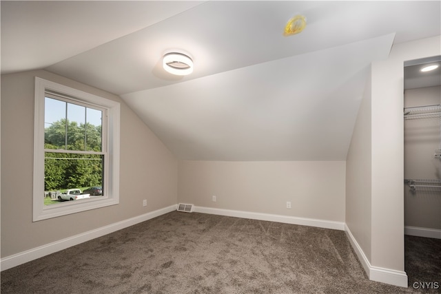 additional living space with dark colored carpet and vaulted ceiling