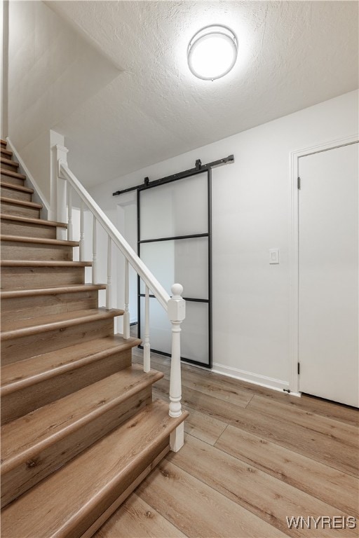 staircase with wood-type flooring, a textured ceiling, and a barn door