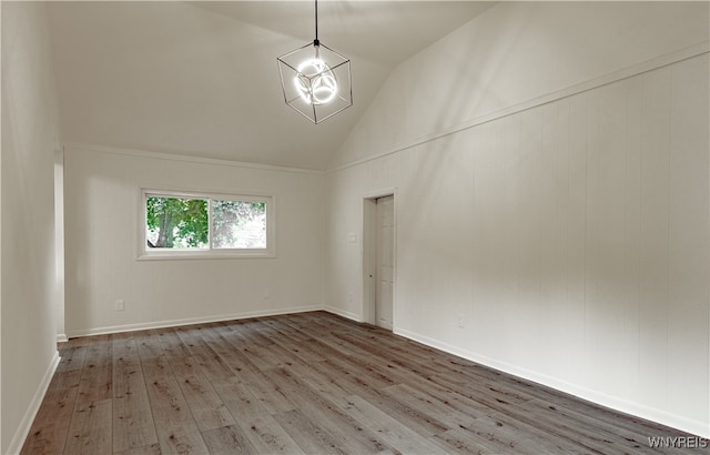 empty room with a notable chandelier, high vaulted ceiling, and hardwood / wood-style flooring