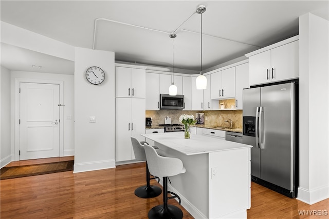 kitchen with appliances with stainless steel finishes, white cabinetry, a center island, and decorative light fixtures