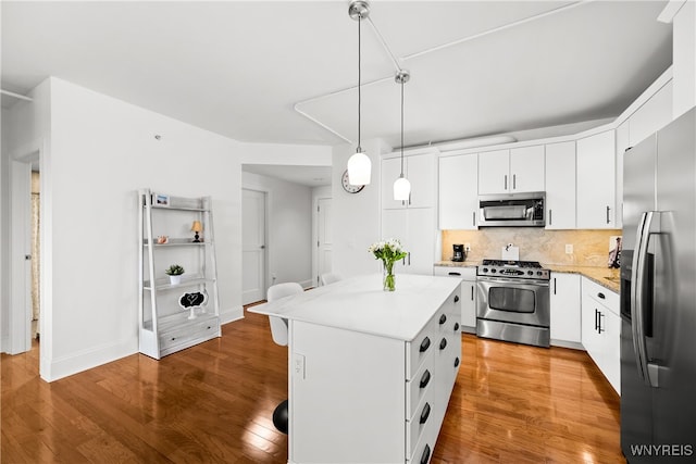 kitchen featuring white cabinets, pendant lighting, stainless steel appliances, wood-type flooring, and a center island