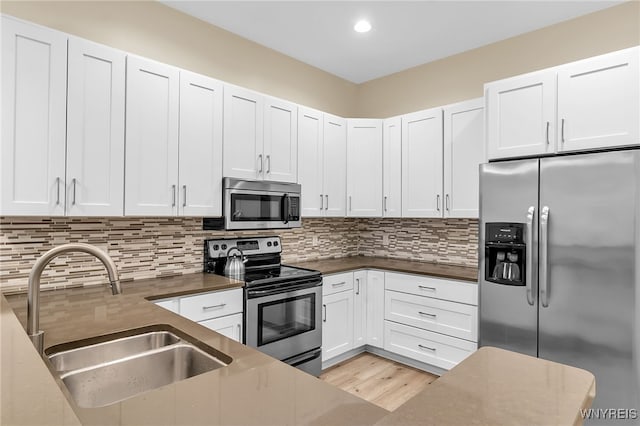 kitchen with tasteful backsplash, sink, white cabinetry, light hardwood / wood-style flooring, and appliances with stainless steel finishes