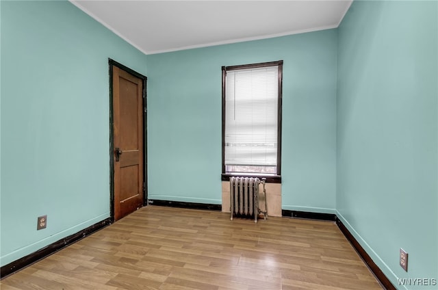 empty room featuring light hardwood / wood-style flooring, radiator, and crown molding