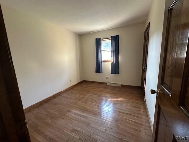 unfurnished room featuring hardwood / wood-style floors and a baseboard radiator