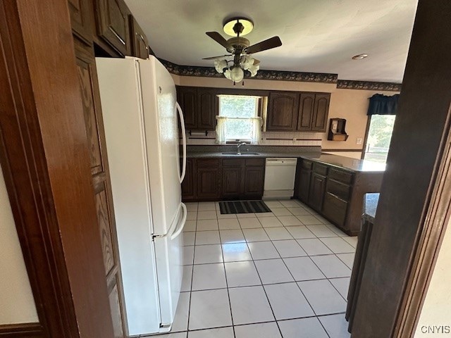 kitchen with white appliances, light tile patterned floors, dark brown cabinets, ceiling fan, and sink