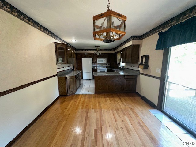 kitchen with dark brown cabinetry, sink, white appliances, light hardwood / wood-style flooring, and a chandelier