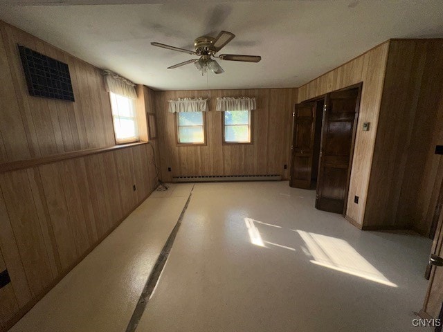 spare room featuring wooden walls, a baseboard heating unit, and ceiling fan