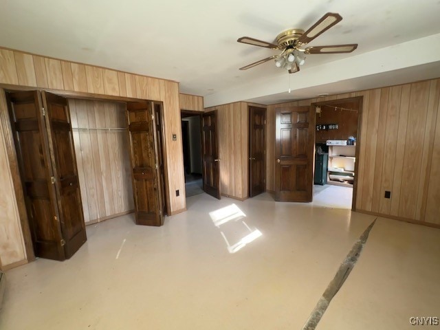 unfurnished bedroom featuring wood walls, ceiling fan, and a closet