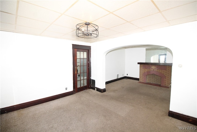 carpeted empty room with a fireplace and a drop ceiling