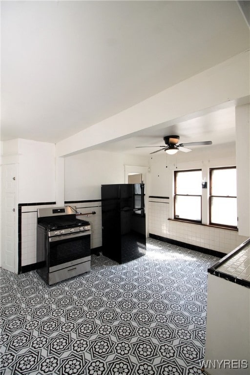 kitchen with tile counters, black fridge, ceiling fan, and stainless steel stove