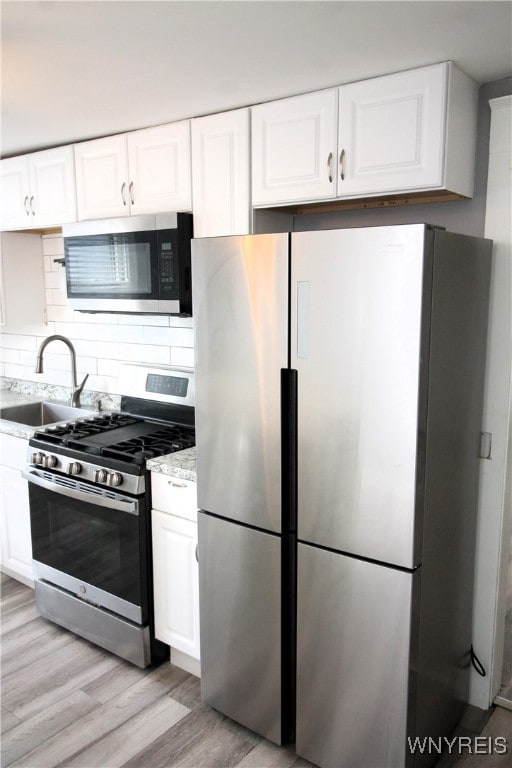 kitchen featuring appliances with stainless steel finishes, light hardwood / wood-style floors, light stone counters, white cabinets, and sink