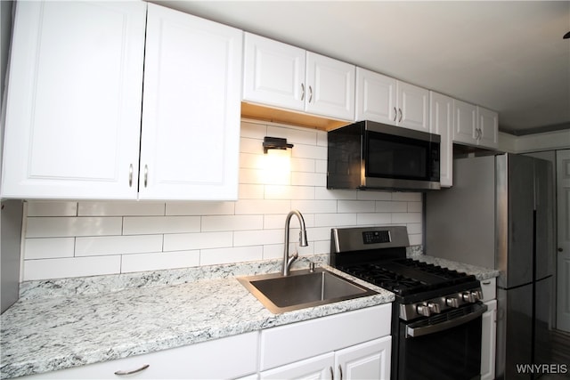 kitchen with tasteful backsplash, white cabinets, light stone countertops, stainless steel appliances, and sink