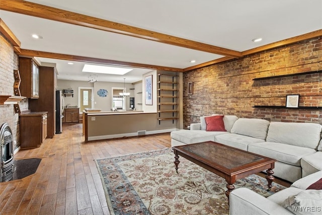 living room featuring beamed ceiling, a wood stove, brick wall, light hardwood / wood-style flooring, and a notable chandelier