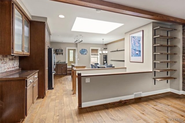 kitchen with stainless steel fridge, hanging light fixtures, light wood-type flooring, an inviting chandelier, and a skylight