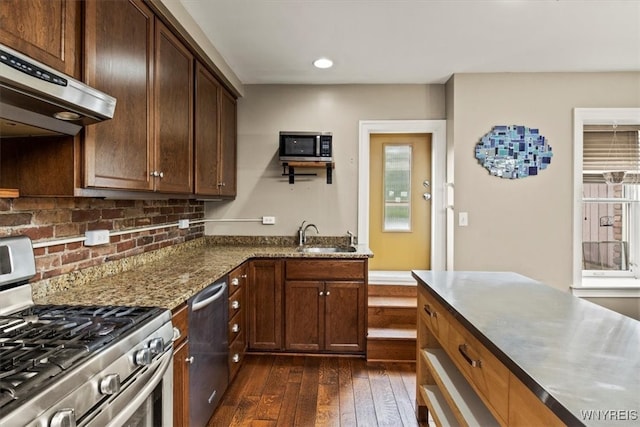 kitchen with sink, appliances with stainless steel finishes, range hood, dark stone countertops, and dark hardwood / wood-style flooring