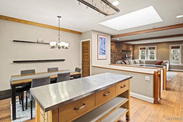 kitchen featuring a skylight, light hardwood / wood-style flooring, decorative light fixtures, stainless steel counters, and a center island