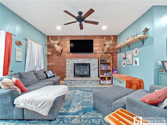 living room featuring ceiling fan, a fireplace, and wood walls