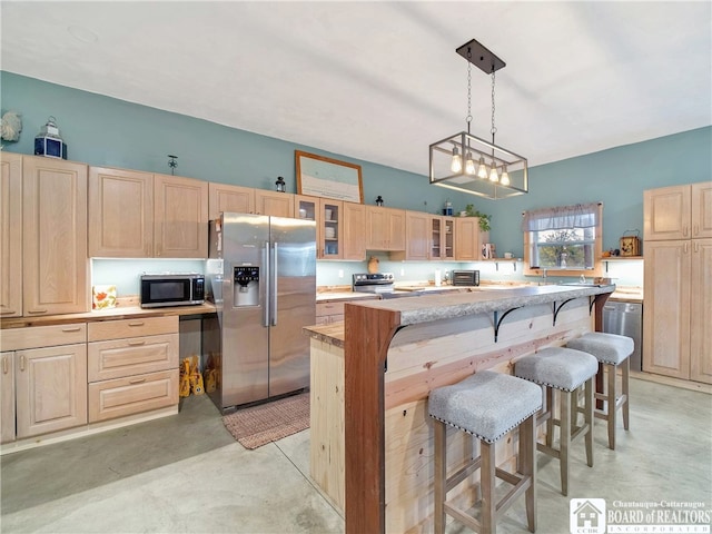 kitchen featuring light brown cabinetry, pendant lighting, stainless steel appliances, and a kitchen breakfast bar