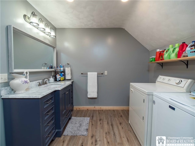 clothes washing area with washing machine and clothes dryer, light wood-type flooring, and sink