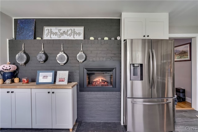 kitchen with dark wood-type flooring, white cabinetry, butcher block counters, a brick fireplace, and stainless steel fridge