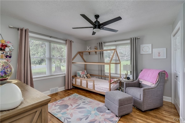 bedroom featuring light hardwood / wood-style flooring, ceiling fan, multiple windows, and a textured ceiling