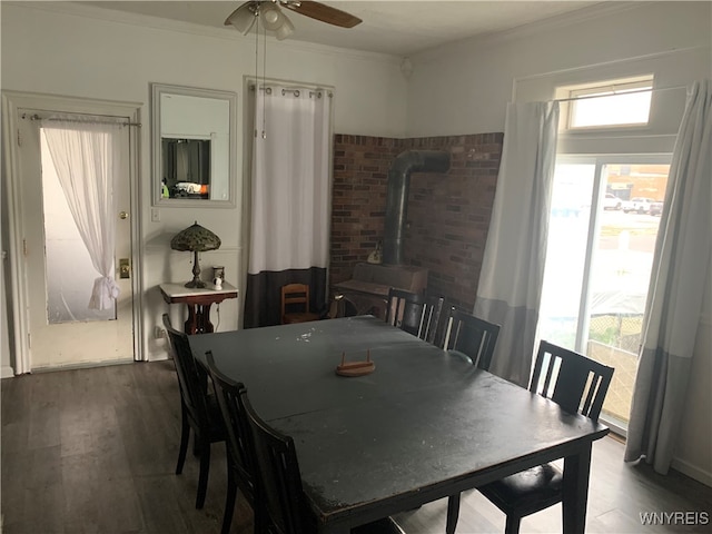 dining room featuring ceiling fan, a wood stove, brick wall, crown molding, and hardwood / wood-style floors