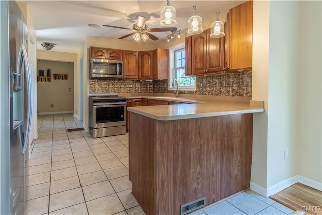 kitchen featuring ceiling fan, pendant lighting, stainless steel appliances, kitchen peninsula, and backsplash