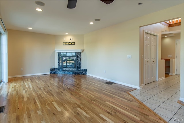 unfurnished living room featuring a high end fireplace, ceiling fan, and light hardwood / wood-style floors