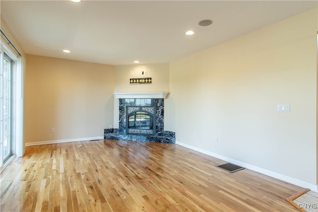 unfurnished living room featuring a premium fireplace, light wood-type flooring, and a healthy amount of sunlight