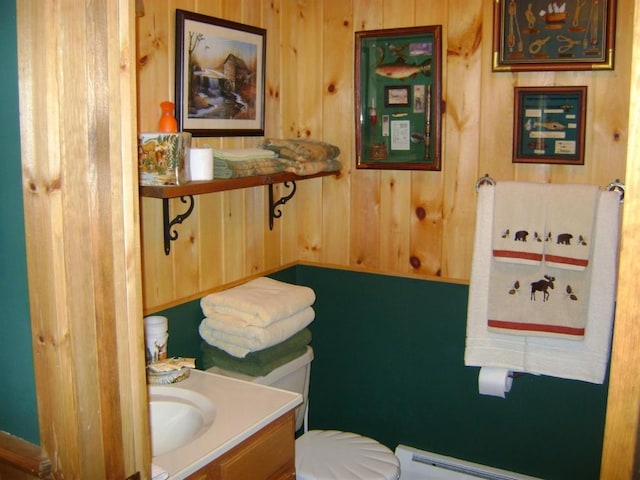 bathroom with a baseboard radiator, wood walls, vanity, and toilet