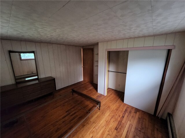 unfurnished bedroom with wooden walls, light hardwood / wood-style flooring, and a baseboard heating unit